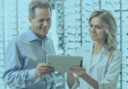 A doctor and patient looking at a tablet in front of a wall of available glasses.